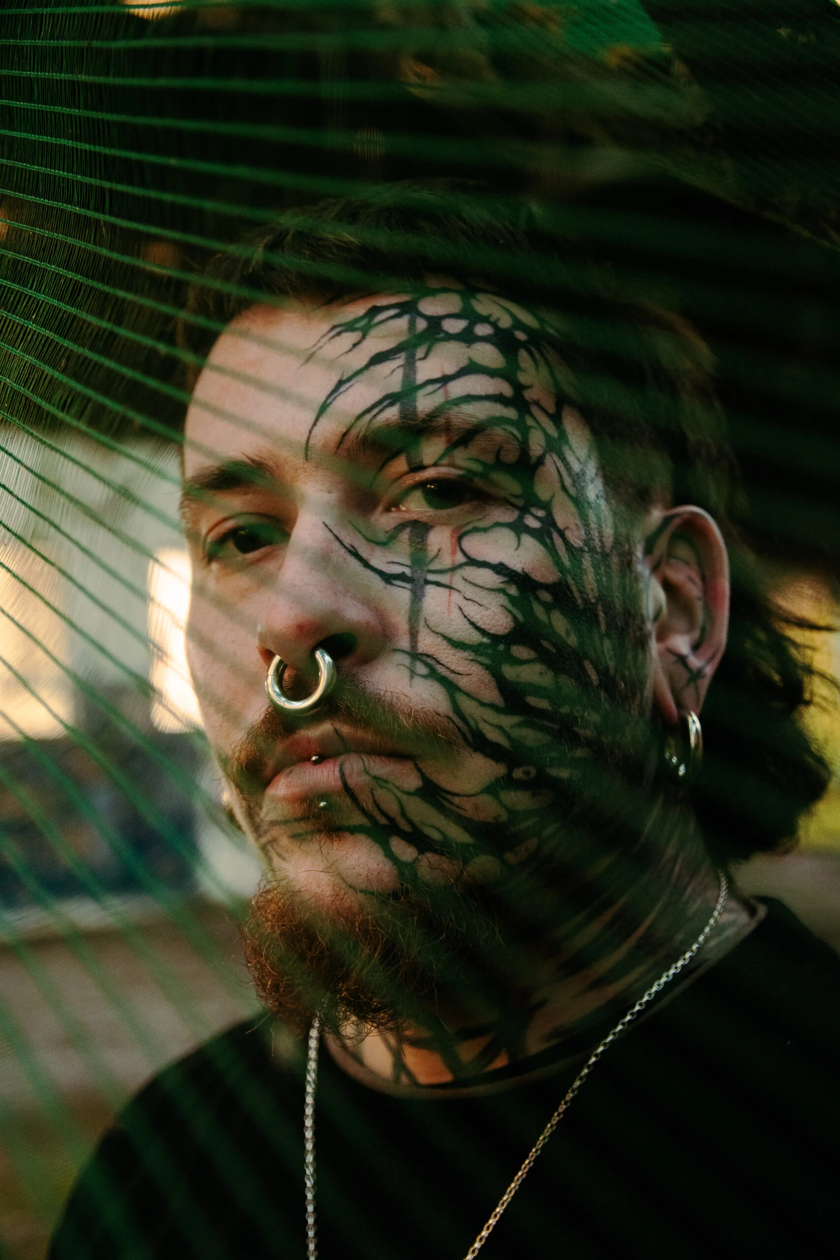 Portrait rapproché d’un homme au visage tatoué, derrière un filet vert