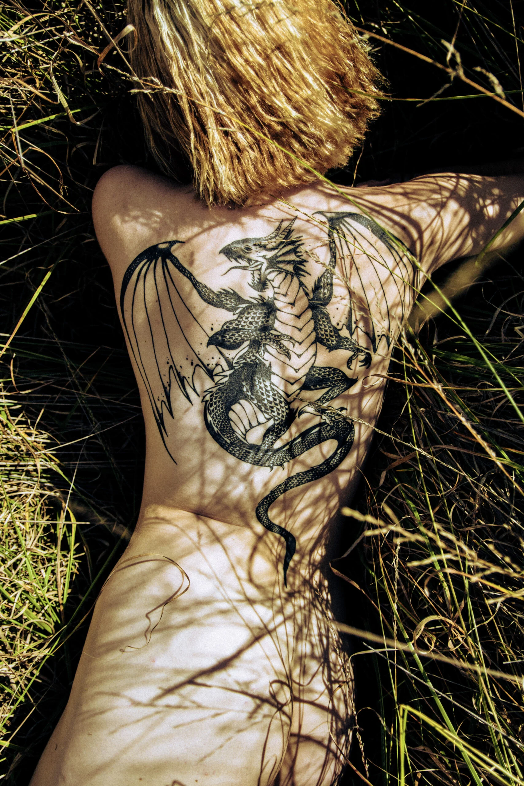 Portrait allongé dans l’herbe, mettant en lumière un tatouage dorsal